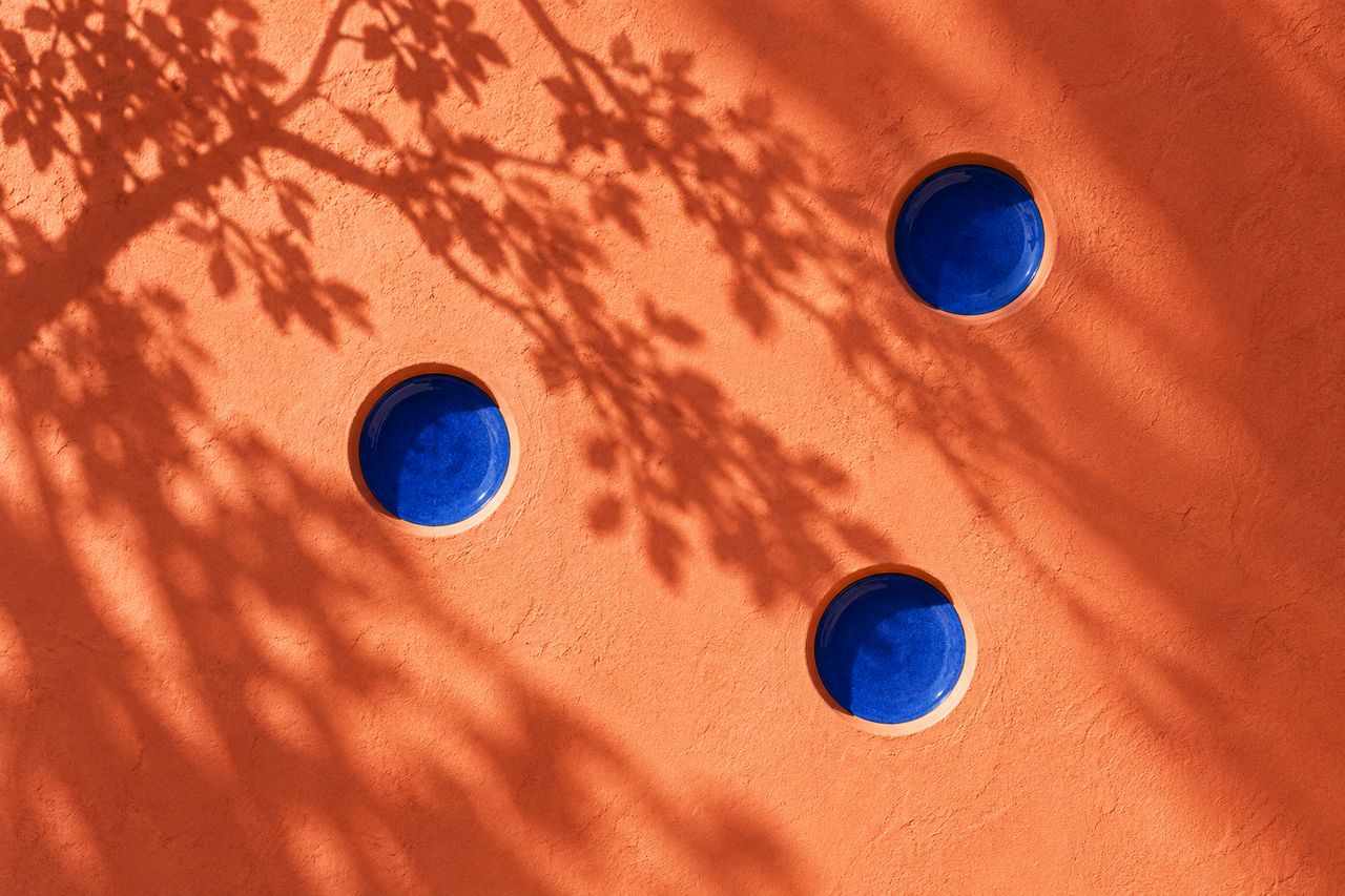 Three blue round insets set into a sunlit coral wall under leafy shadows